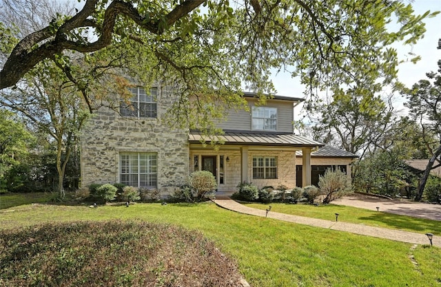 view of front facade with metal roof, stone siding, driveway, a standing seam roof, and a front yard