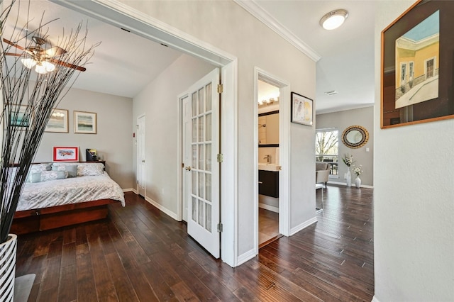 bedroom featuring dark wood-style floors, crown molding, ensuite bath, and baseboards