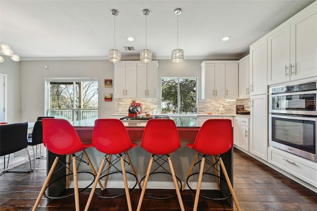 kitchen featuring visible vents, white cabinets, a kitchen island, a breakfast bar area, and double oven