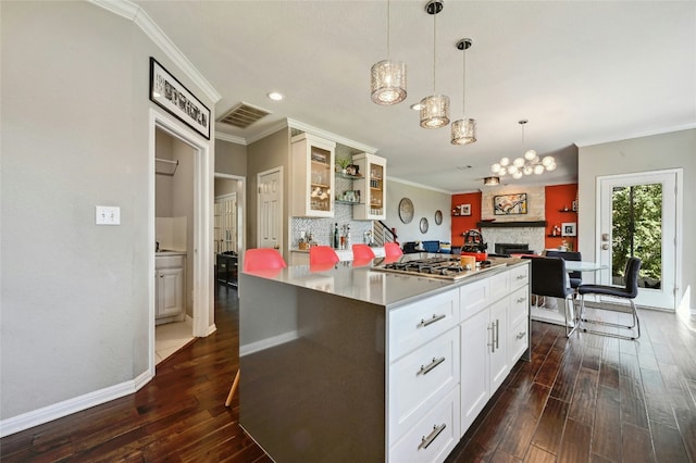 kitchen featuring a center island, visible vents, backsplash, dark wood-type flooring, and glass insert cabinets