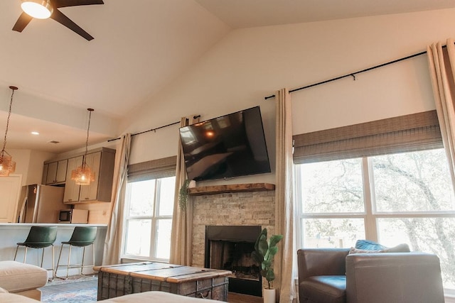 living room featuring ceiling fan, a fireplace, and vaulted ceiling