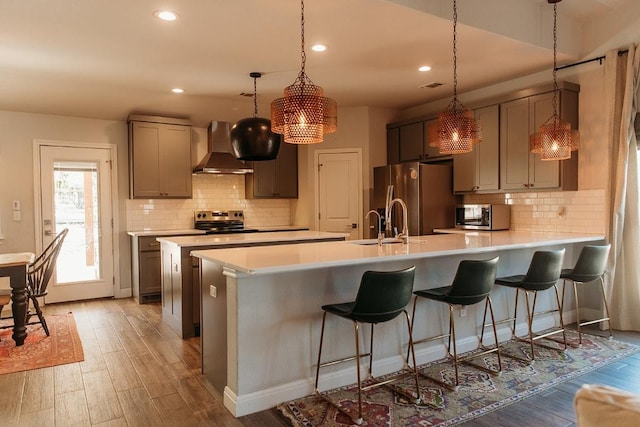 kitchen featuring stainless steel appliances, light countertops, light wood-style flooring, and wall chimney exhaust hood