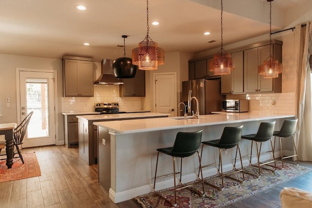kitchen with tasteful backsplash, wall chimney range hood, appliances with stainless steel finishes, and light wood-style floors