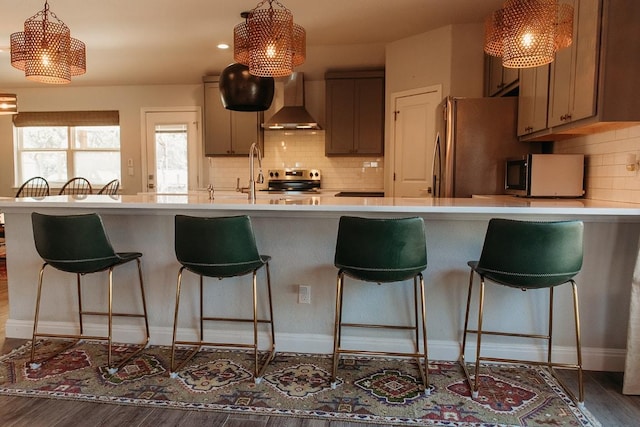 kitchen featuring light countertops, wood finished floors, wall chimney range hood, and stainless steel appliances