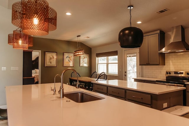 kitchen featuring visible vents, stainless steel electric stove, light countertops, wall chimney range hood, and a sink