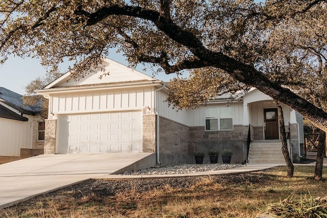 ranch-style home featuring concrete driveway, stone siding, an attached garage, and board and batten siding