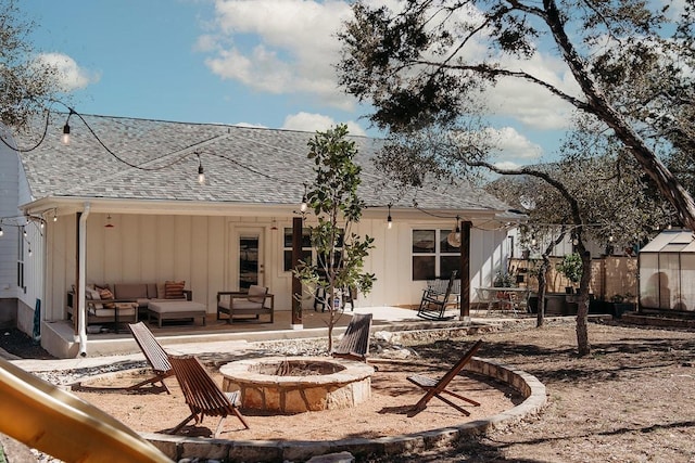 rear view of property with an outdoor living space with a fire pit, roof with shingles, board and batten siding, a patio area, and fence