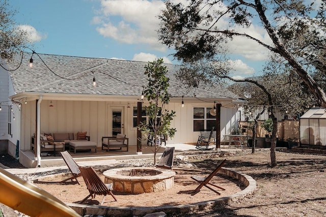 rear view of house with a patio, roof with shingles, board and batten siding, an outdoor living space with a fire pit, and fence