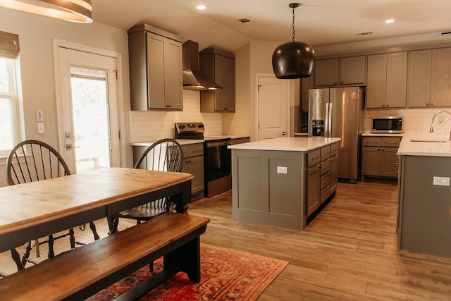 kitchen with light wood-style flooring, recessed lighting, light countertops, appliances with stainless steel finishes, and wall chimney exhaust hood