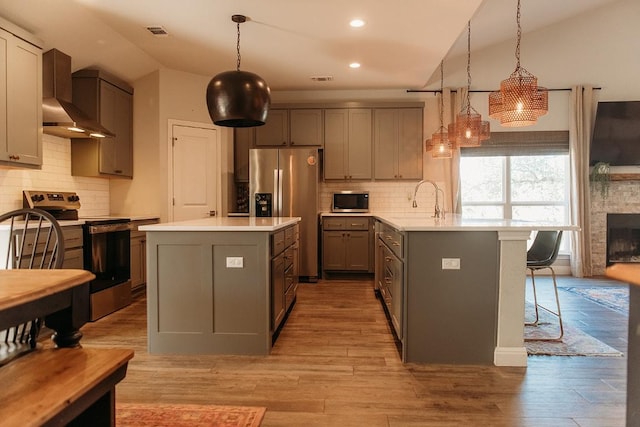 kitchen with appliances with stainless steel finishes, gray cabinetry, wall chimney range hood, and an island with sink