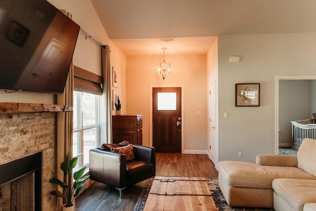 foyer entrance featuring a notable chandelier, visible vents, a stone fireplace, wood finished floors, and baseboards