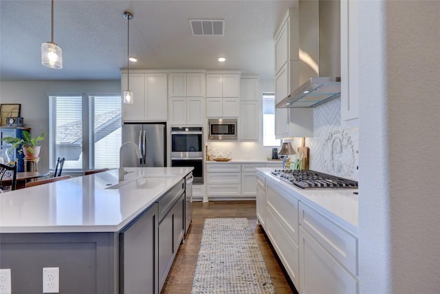 kitchen featuring visible vents, wall chimney range hood, tasteful backsplash, appliances with stainless steel finishes, and light countertops