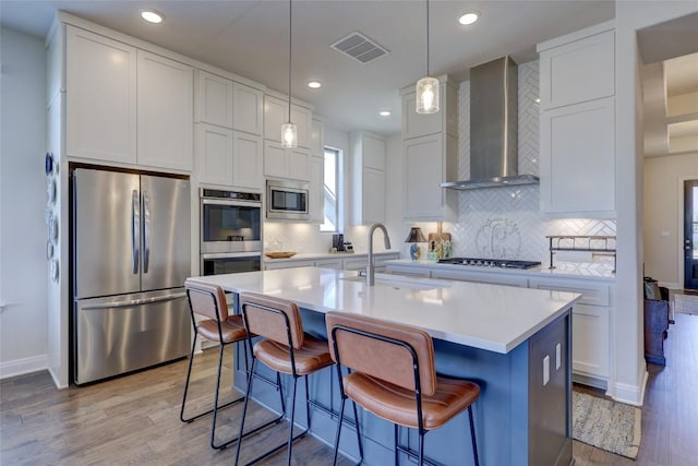 kitchen featuring visible vents, a sink, wall chimney range hood, appliances with stainless steel finishes, and light countertops