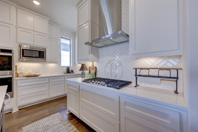 kitchen featuring backsplash, wall chimney range hood, light countertops, stainless steel appliances, and white cabinetry