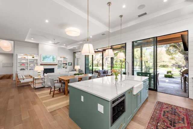 kitchen with a wealth of natural light, green cabinets, a fireplace, light wood finished floors, and a raised ceiling