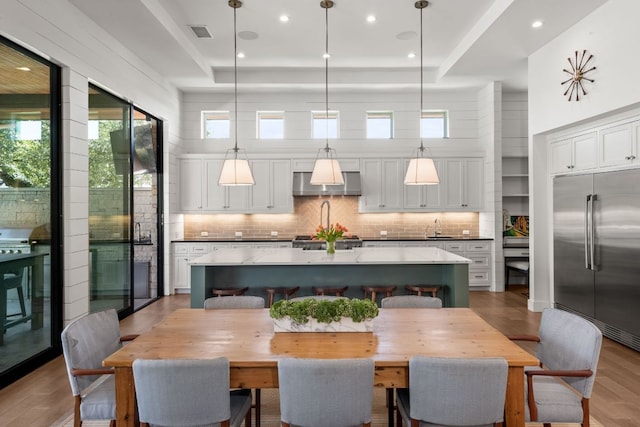 dining room featuring wood finished floors, visible vents, recessed lighting, a towering ceiling, and a raised ceiling