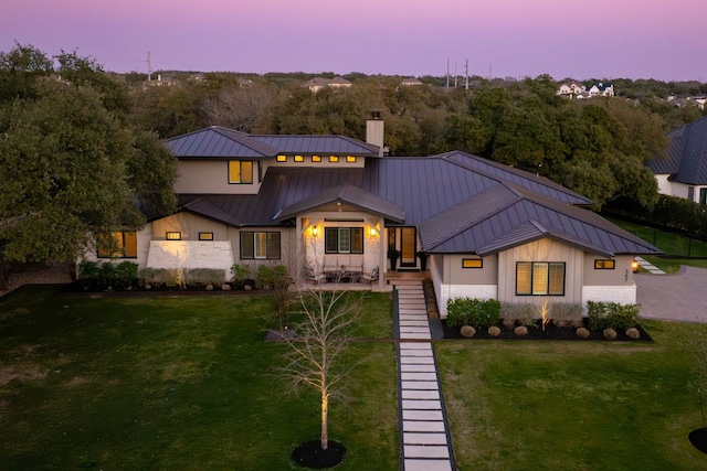 modern farmhouse featuring a standing seam roof, a front lawn, a chimney, and metal roof