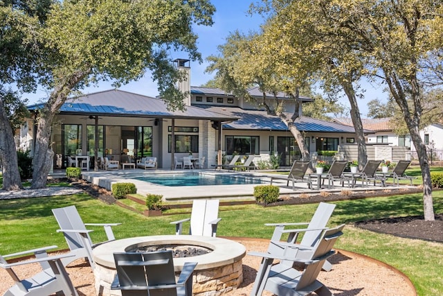 back of property with a patio, an outdoor fire pit, a standing seam roof, an outdoor pool, and metal roof