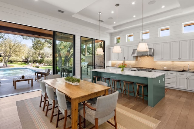 dining space featuring visible vents, recessed lighting, a high ceiling, light wood-style floors, and a raised ceiling