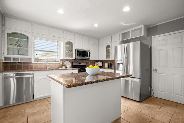 kitchen featuring white cabinets, appliances with stainless steel finishes, tasteful backsplash, dark stone countertops, and glass insert cabinets