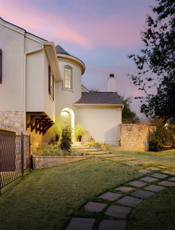 view of side of property with stucco siding, a yard, a chimney, and fence