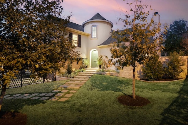 french provincial home featuring fence, a lawn, and stucco siding