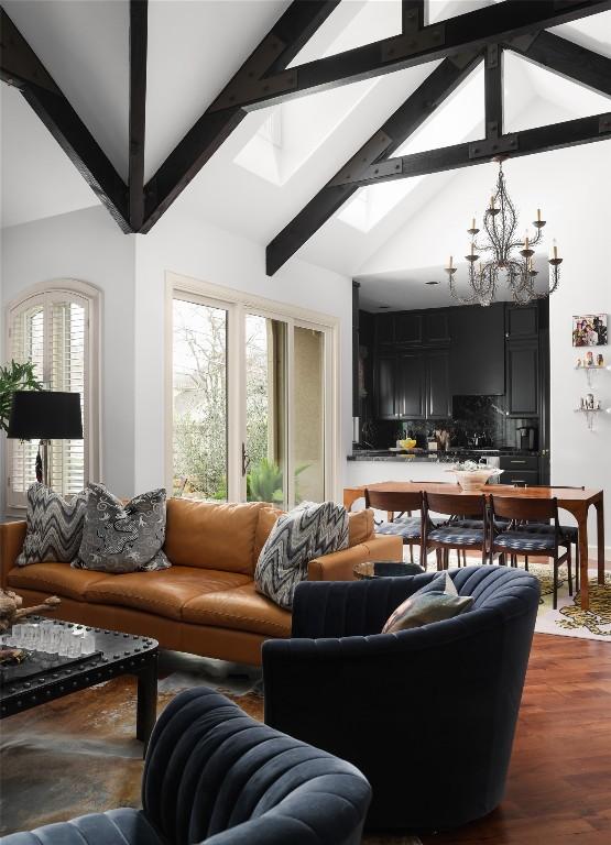 living room featuring beamed ceiling, high vaulted ceiling, a notable chandelier, a skylight, and dark wood-style flooring