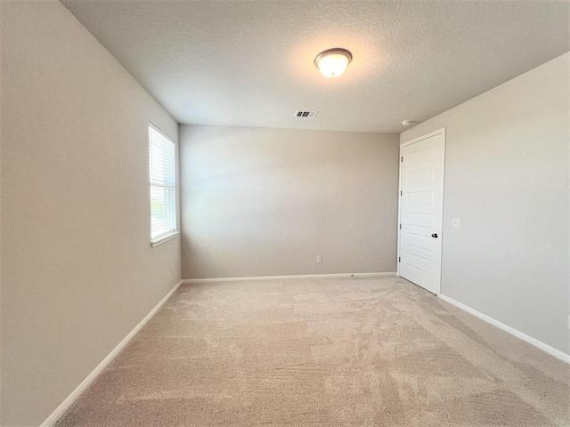 unfurnished room with light carpet, a textured ceiling, visible vents, and baseboards