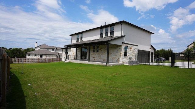 rear view of house with a garage, driveway, a lawn, stone siding, and fence private yard