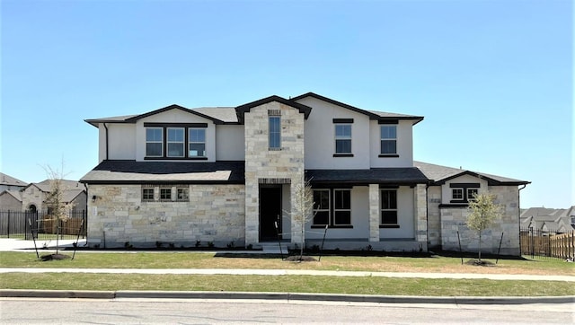 view of front of property with stucco siding, a shingled roof, fence, stone siding, and a front lawn