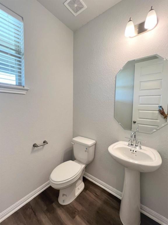 half bathroom featuring toilet, wood finished floors, visible vents, and baseboards