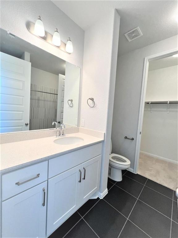 bathroom featuring visible vents, a spacious closet, toilet, vanity, and tile patterned floors