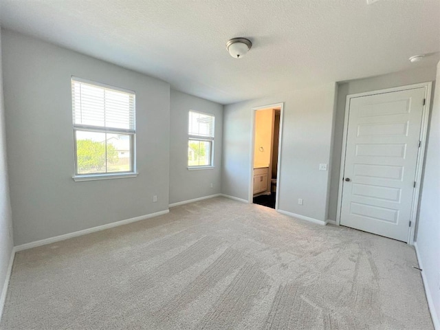 unfurnished bedroom with carpet, a textured ceiling, baseboards, and ensuite bathroom