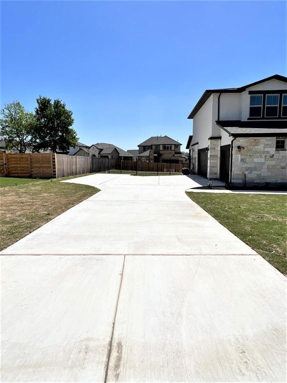 view of property exterior with a garage, driveway, stone siding, fence, and stucco siding