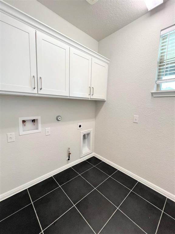 laundry area with hookup for an electric dryer, hookup for a gas dryer, dark tile patterned floors, baseboards, and cabinet space