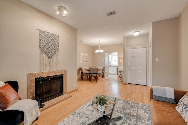 living area featuring a textured ceiling, a notable chandelier, wood finished floors, visible vents, and a tiled fireplace