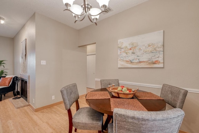 dining space with a fireplace, visible vents, baseboards, light wood-type flooring, and an inviting chandelier