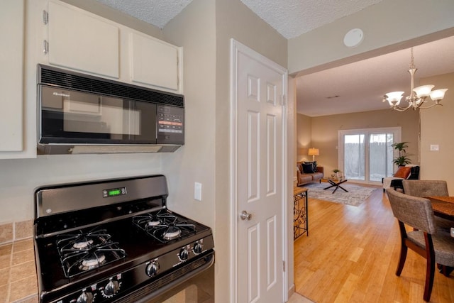 kitchen featuring range with gas cooktop, an inviting chandelier, light wood-style floors, white cabinetry, and black microwave