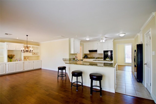 kitchen featuring dark wood finished floors, decorative backsplash, ornamental molding, a peninsula, and black appliances