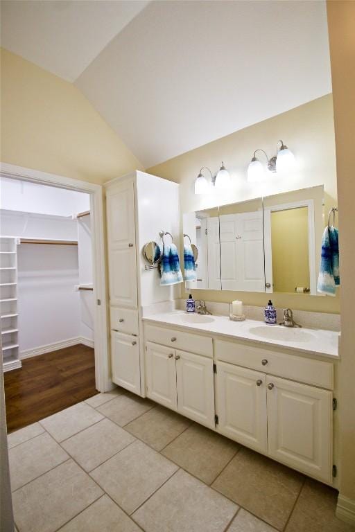 full bathroom featuring tile patterned floors, vaulted ceiling, a sink, and double vanity