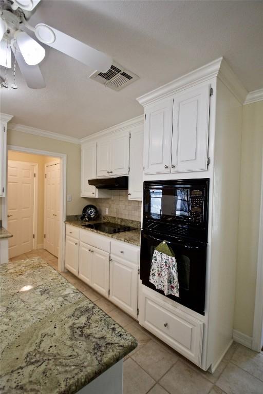 kitchen with crown molding, visible vents, light stone countertops, under cabinet range hood, and black appliances