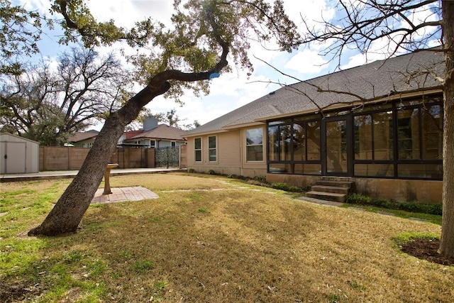 rear view of property featuring an outbuilding, a lawn, a sunroom, fence, and a shed