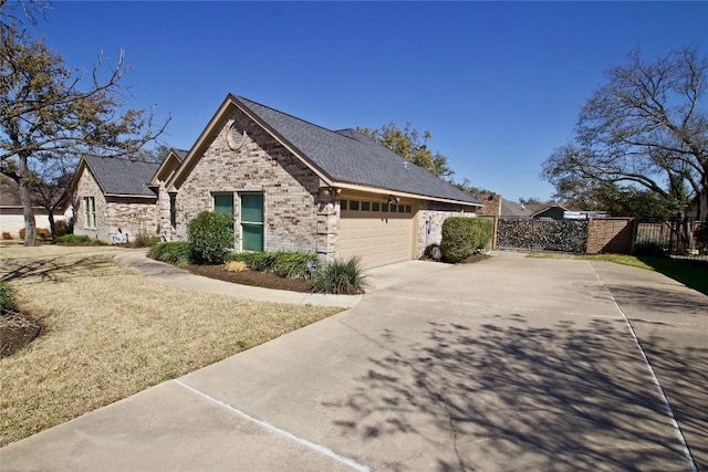 view of side of home featuring a garage, brick siding, fence, concrete driveway, and a gate