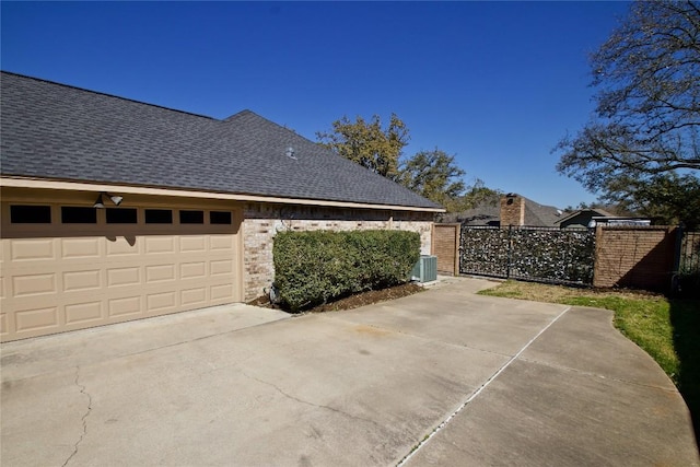 view of side of property featuring a shingled roof, a gate, central AC, fence, and driveway