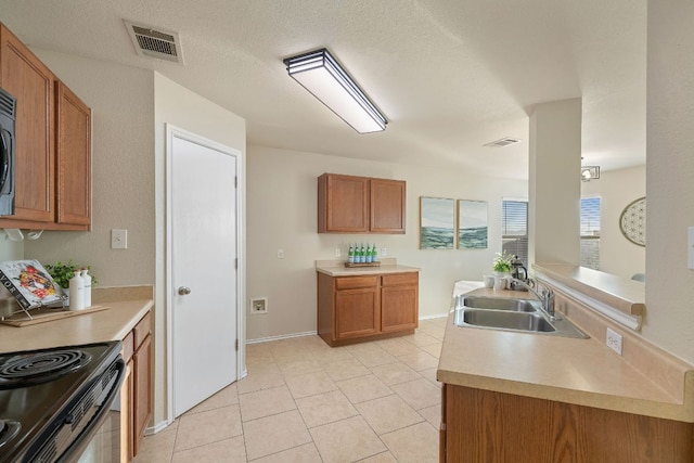 kitchen featuring light countertops, brown cabinetry, a sink, and visible vents