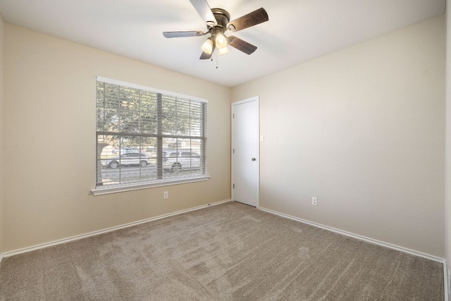 carpeted spare room featuring baseboards and a ceiling fan