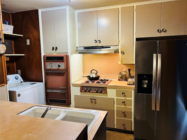 kitchen with light countertops, wall oven, washer / dryer, stainless steel fridge, and under cabinet range hood