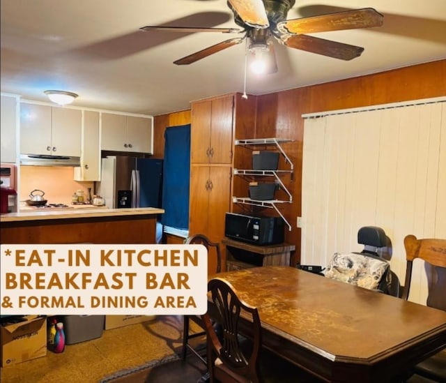 interior space featuring range hood, a ceiling fan, wood walls, black microwave, and stainless steel fridge