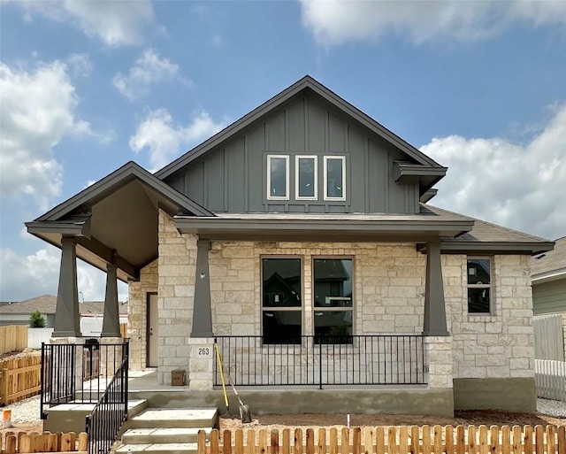 view of front of property with covered porch, board and batten siding, stone siding, and fence