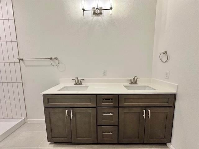 bathroom with a tile shower, tile patterned floors, double vanity, and baseboards